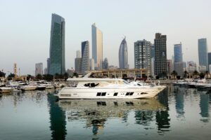 Stunning view of modern skyline in Kuwait City with yachts reflecting on marina waters.