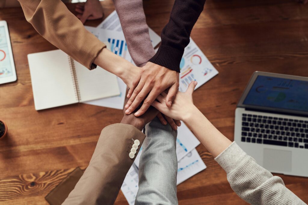 About Us Diverse professionals unite for teamwork around a wooden table with laptops and documents.