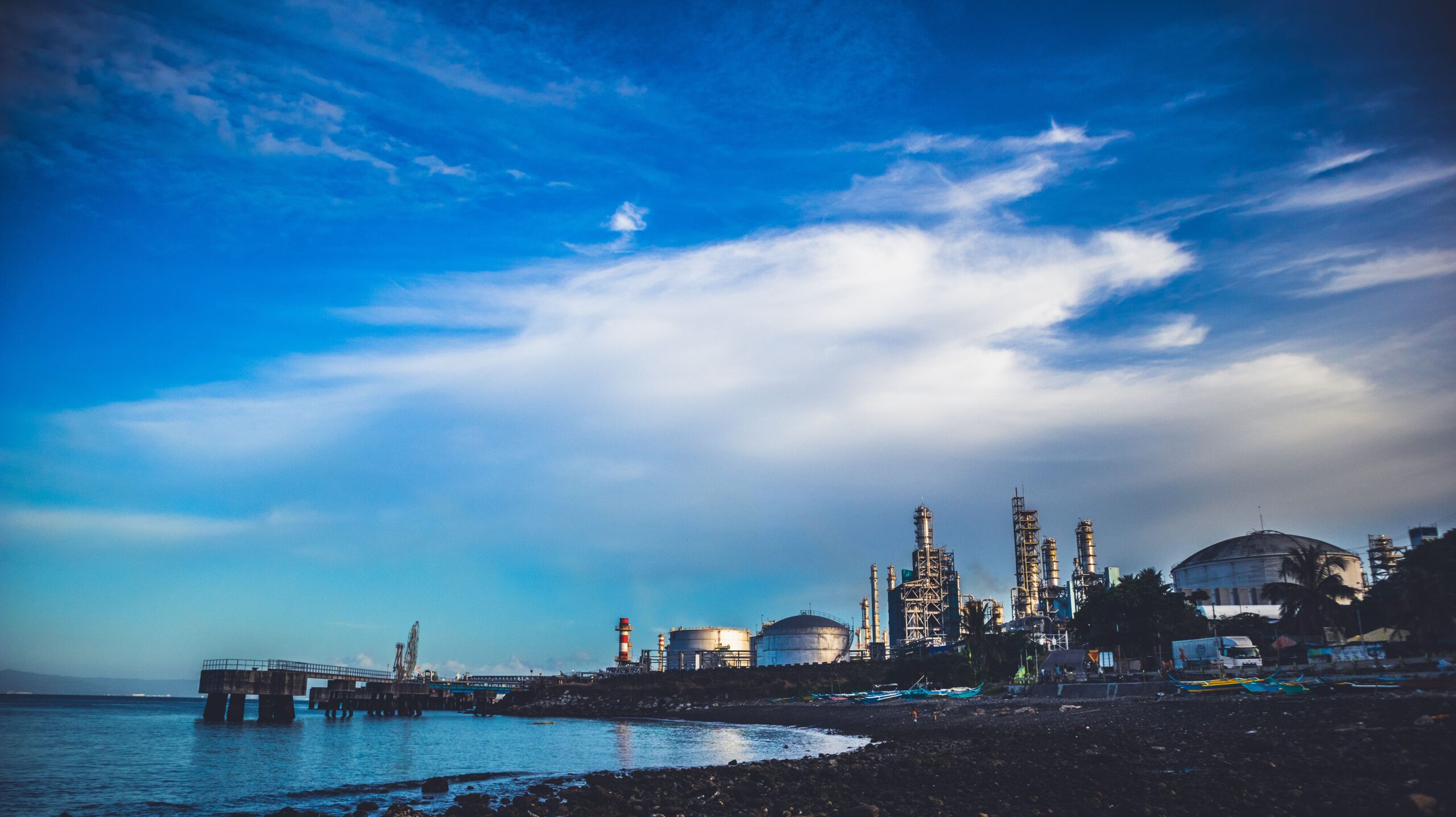 EW/0012 – Replacement of 12” Crude Oil Line with 16” Crude Oil Line and Associated Facilities Industrial buildings by the sea under a dramatic cloudy sky.