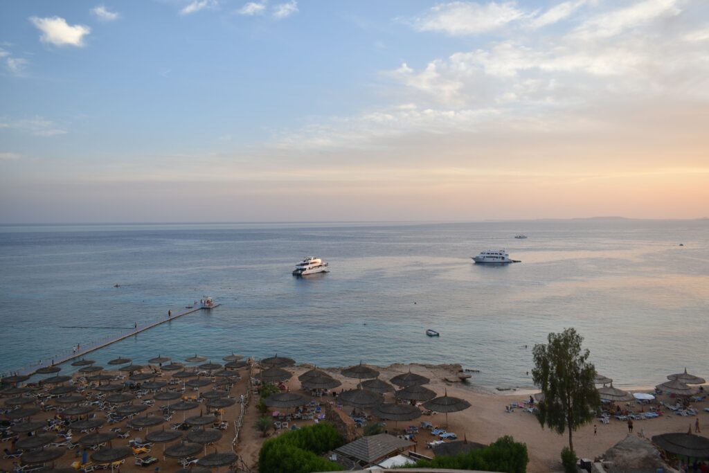 Stunning aerial view of Sharm El Sheikh's beach and sea during sunset with boats and parasols.