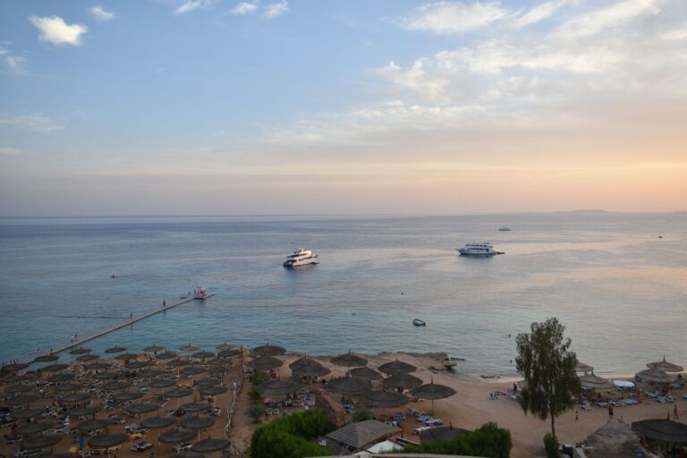 Stunning aerial view of Sharm El Sheikh's beach and sea during sunset with boats and parasols.