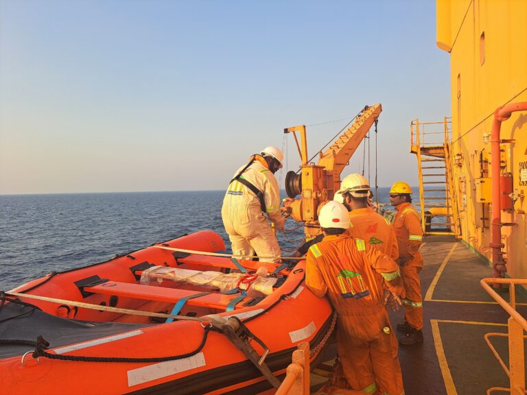 Crew members in protective gear ready a lifeboat during an offshore safety drill on a ship.