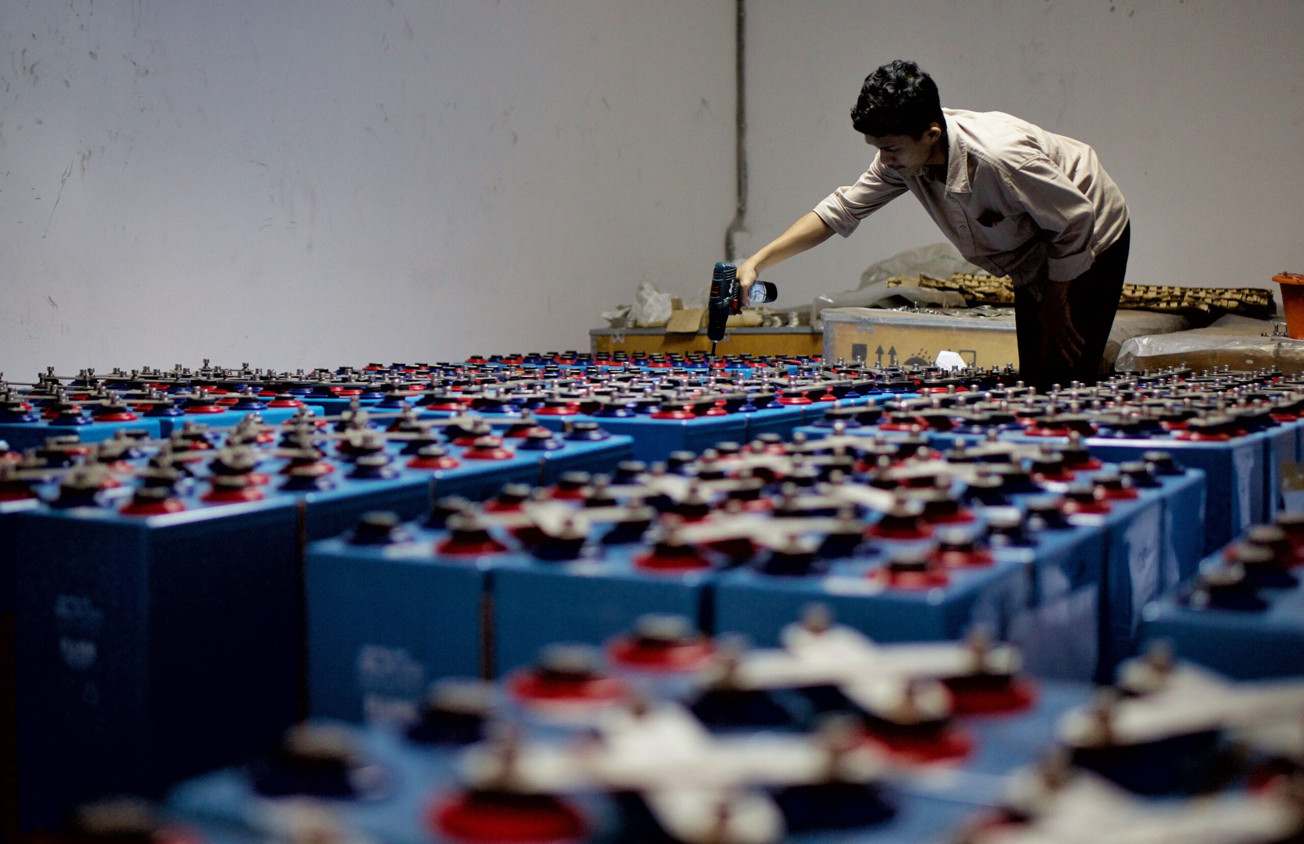 EIA for Ibn El Nafees Battery Recycling Facility A worker checking many industrial batteries inside a facility. Indoor, industrial setting.