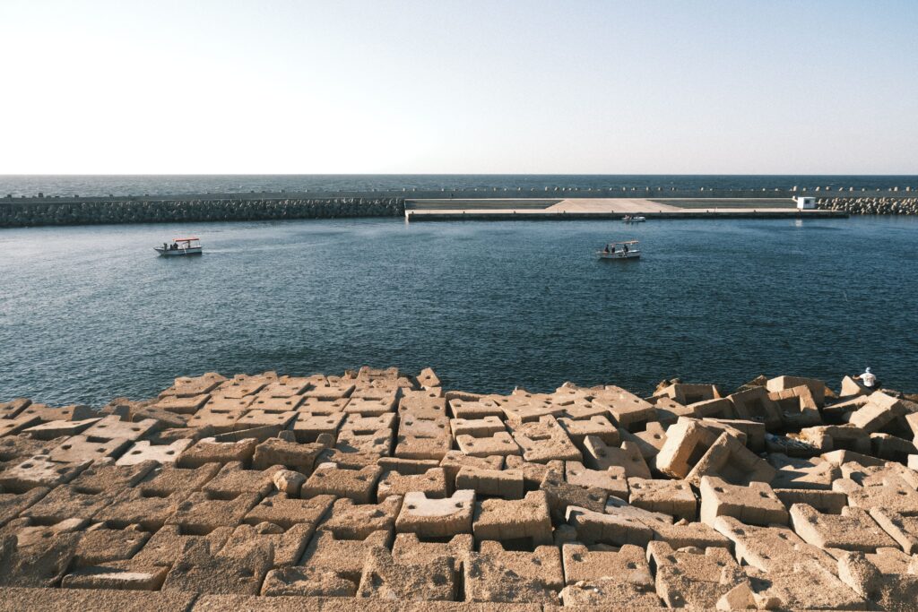 Tranquil scene of boats near a stone breakwater in Alexandria harbor under a clear sky.