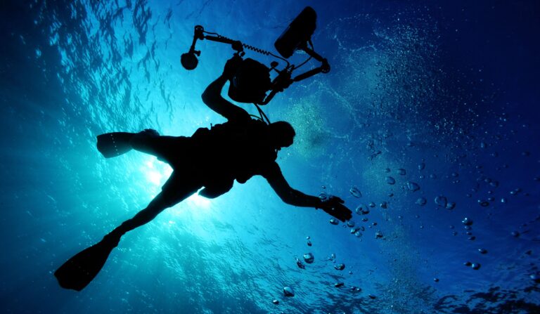 Site Inspection Using ROV for the High Dam, Aswan Silhouette of a diver filming underwater, capturing the serene oceanic environment.